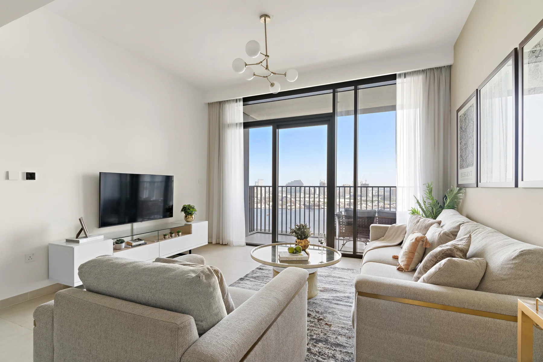 A bright living room with seating, a television, and large windows opening onto a balcony.