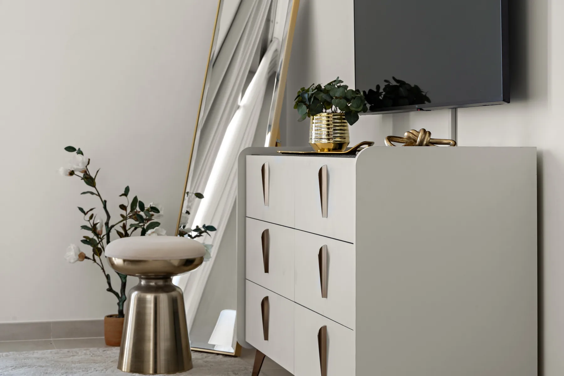A bedroom dresser and television stand beside a full-length mirror and potted plant.
