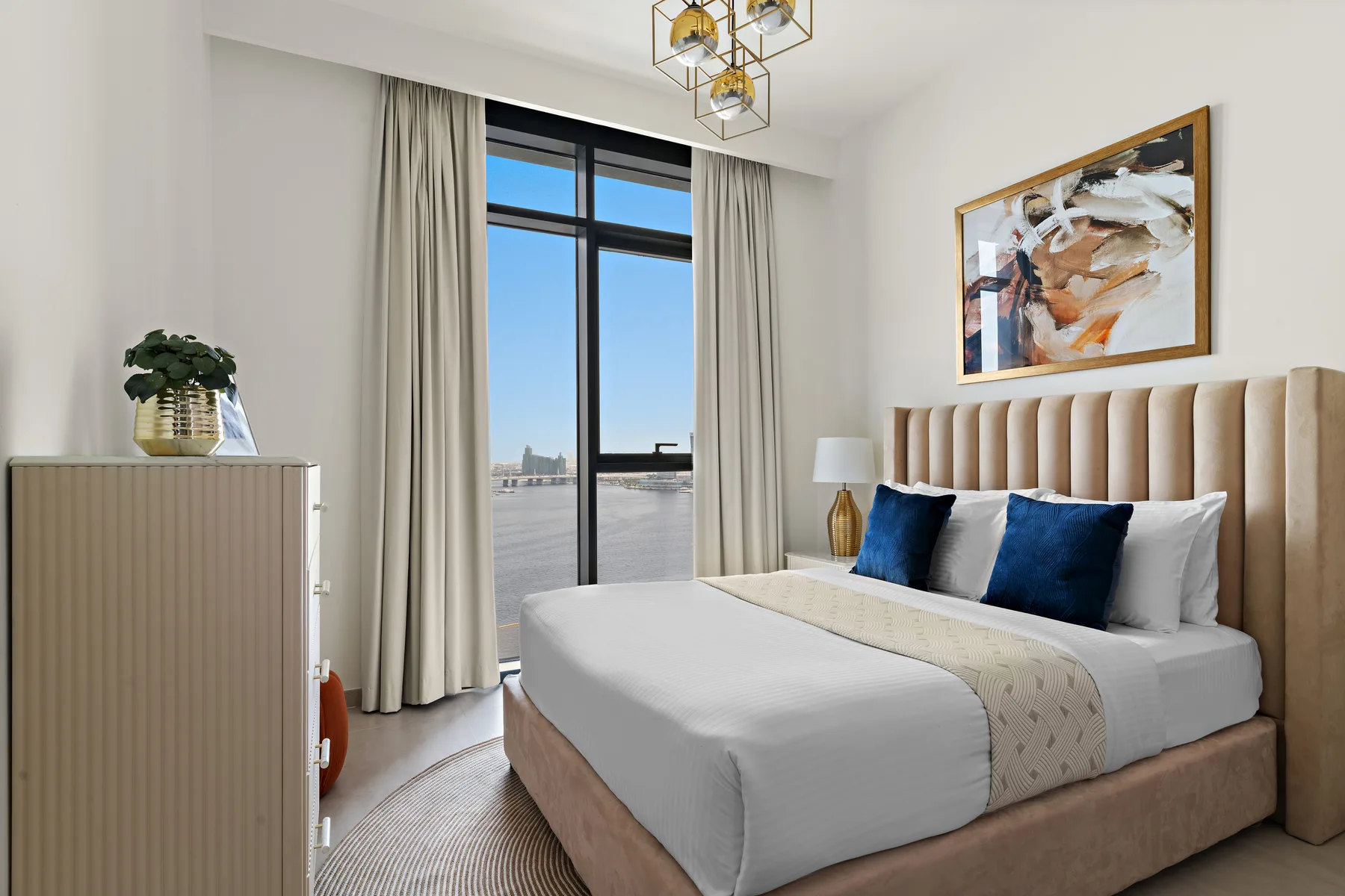 A bedroom with a neatly made bed, blue pillows, and a large window.