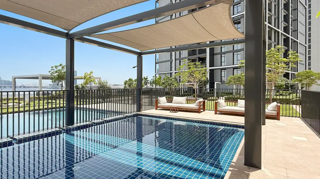 An outdoor swimming pool sits beneath shade canopies beside a modern building.