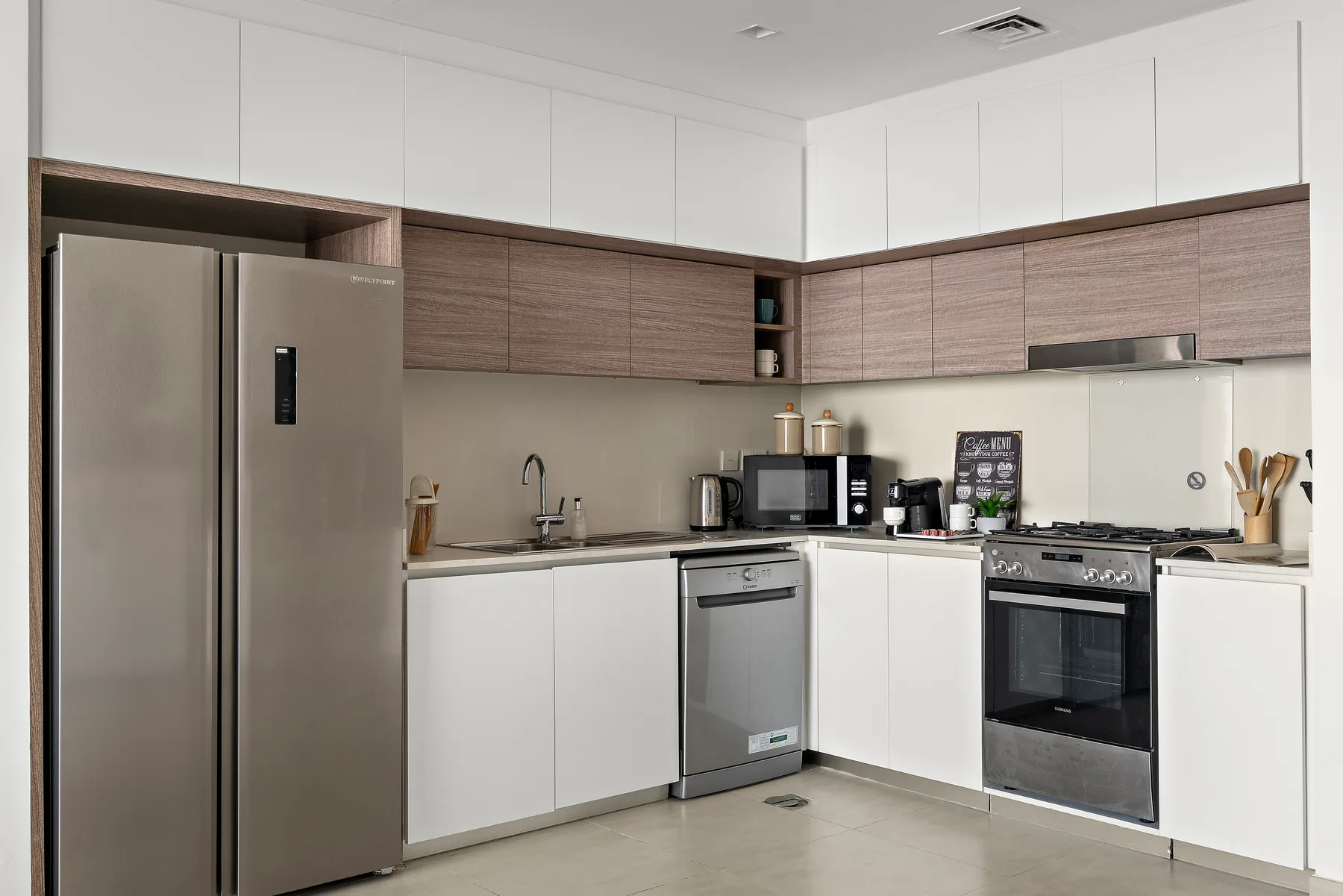 A modern kitchen with white cabinets, wood-toned cupboards, and stainless steel appliances.