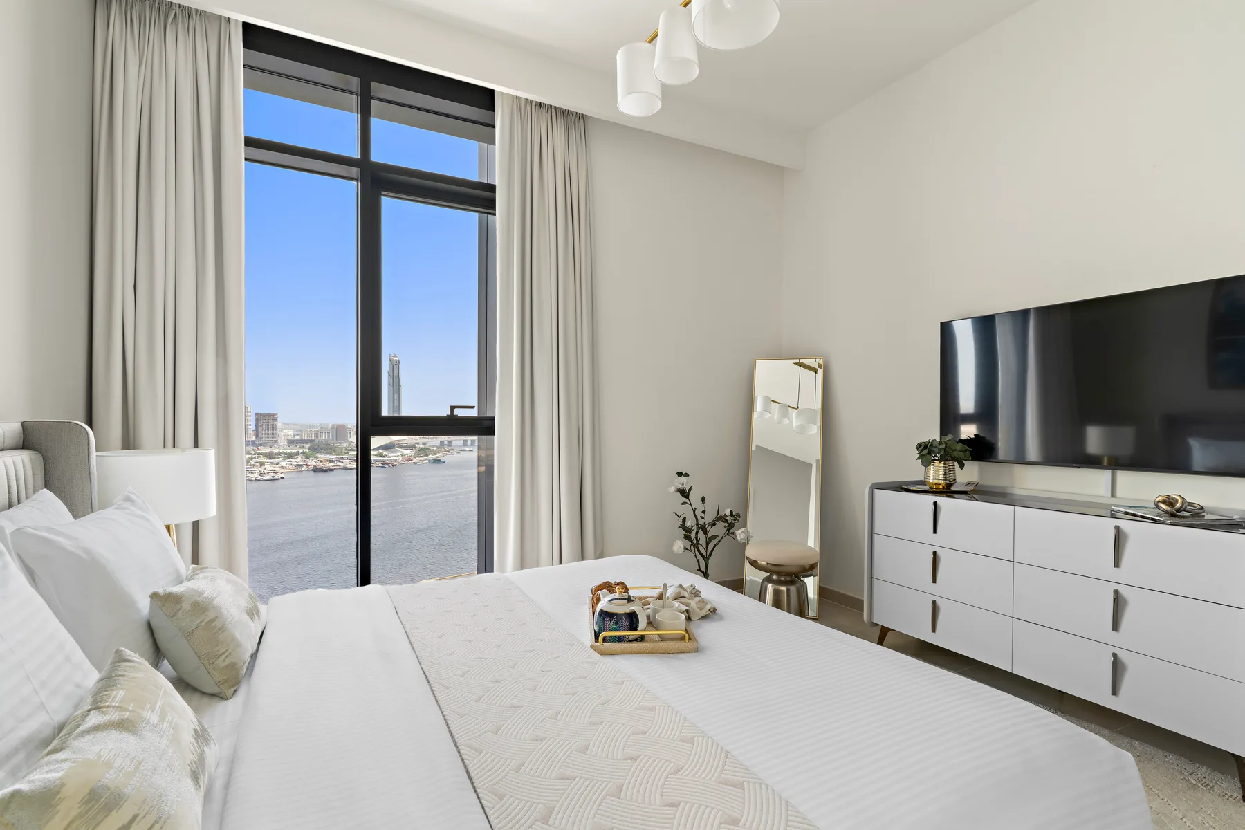 A bright bedroom with a large window overlooking the water and a television.