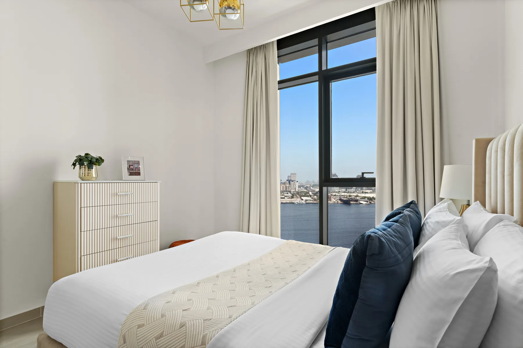 A bright bedroom with a large bed facing a tall window overlooking the water.