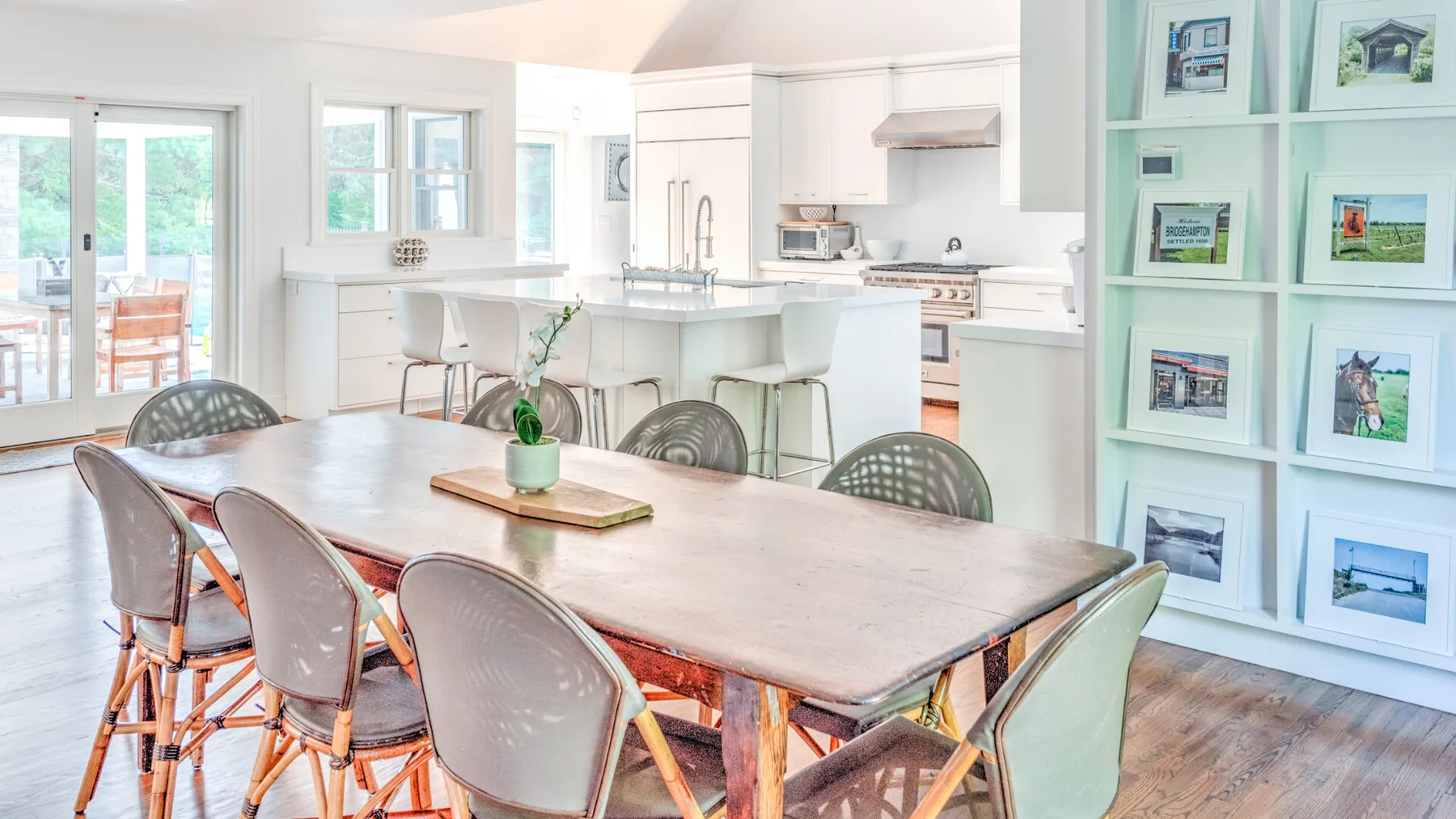 Un comedor luminoso y abierto con una mesa larga junto a una cocina blanca.