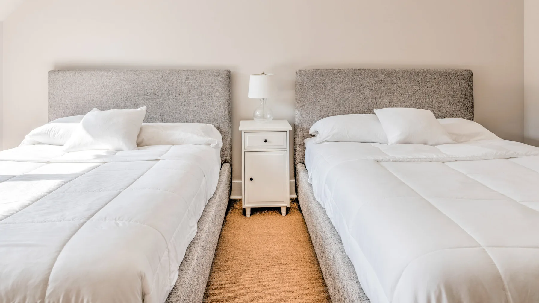 Un dormitorio luminoso con dos camas y una mesita de noche entre ellas.