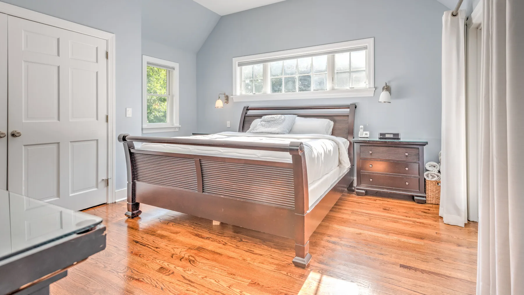 Un dormitorio con una cama de madera, muebles junto a la cama y cortinas claras.