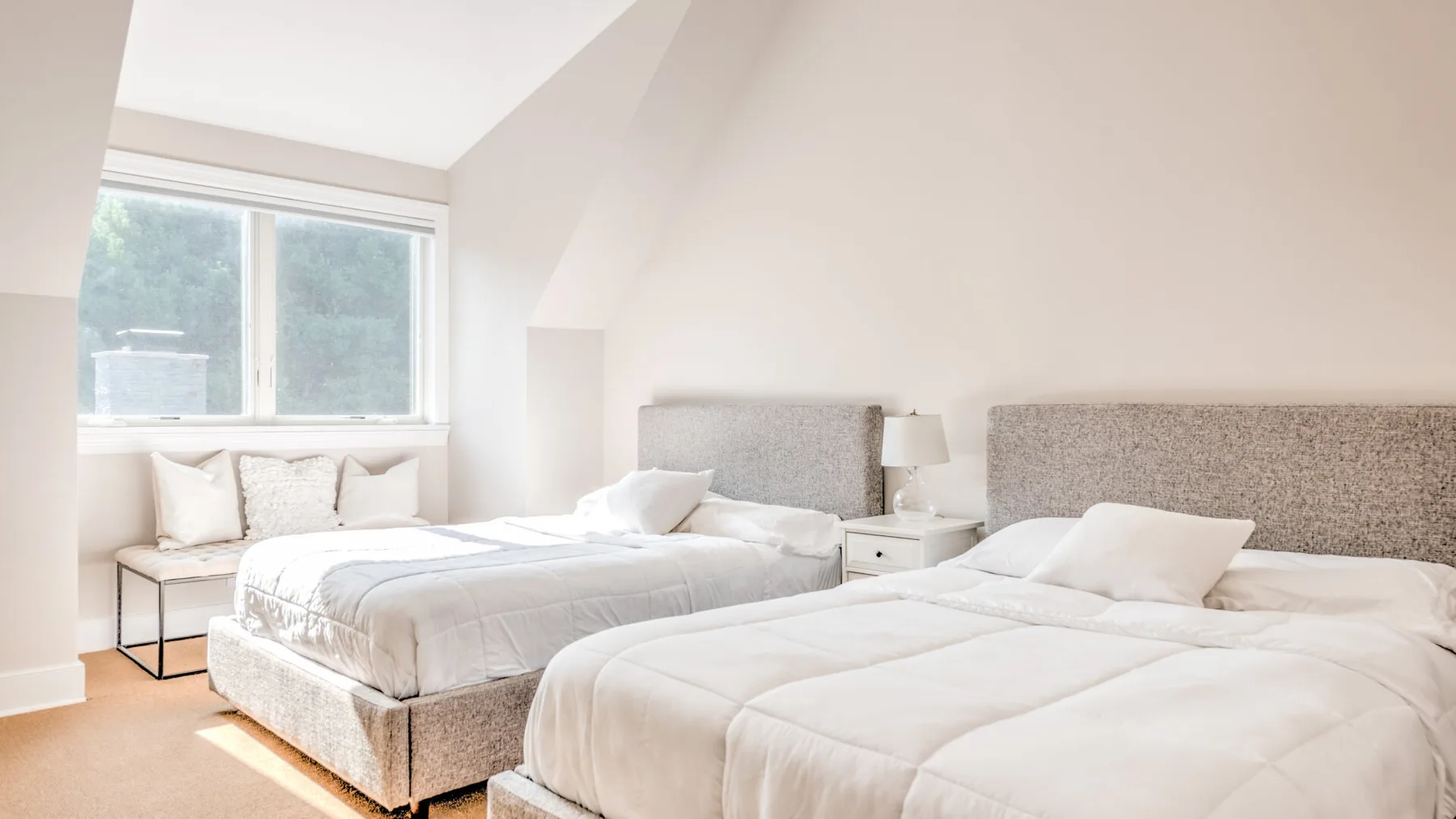 Un dormitorio luminoso con dos camas junto a una ventana grande.
