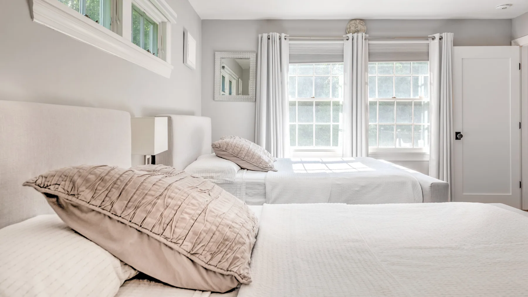 Un dormitorio luminoso con dos camas y ventanas grandes.