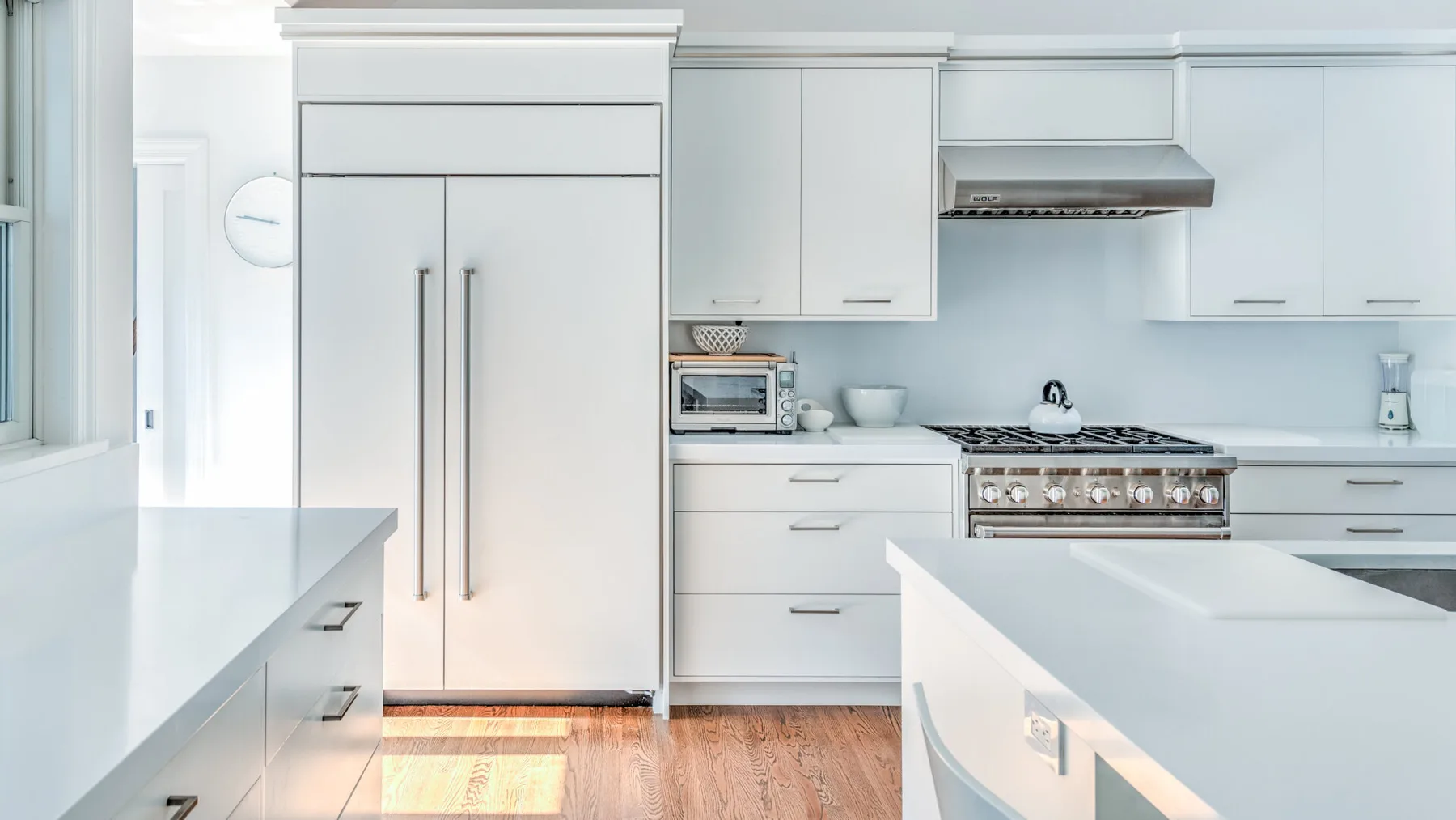 Una cocina blanca y luminosa con una isla central y una estufa de acero inoxidable.