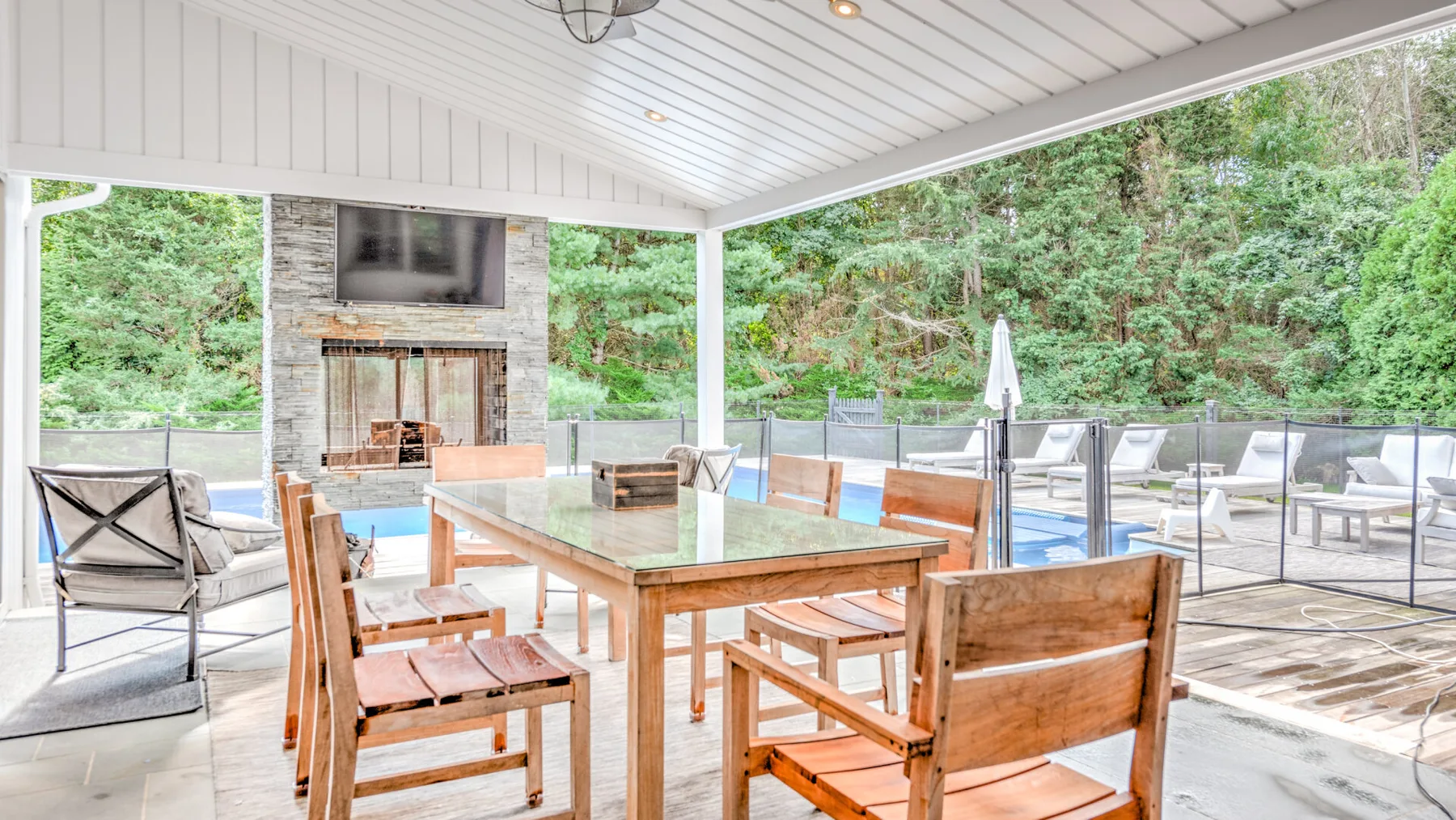 Un comedor exterior cubierto con mesa de madera y asientos da a un patio arbolado.