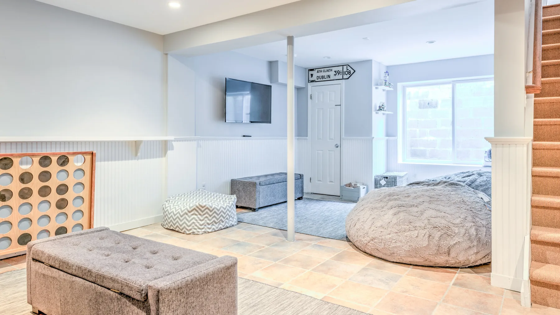 Una luminosa habitación en el sótano con televisor, asientos acolchados y una ventana grande.