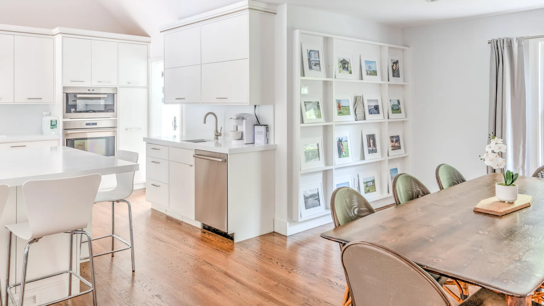 Una luminosa cocina con comedor, armarios blancos y una larga mesa de madera.