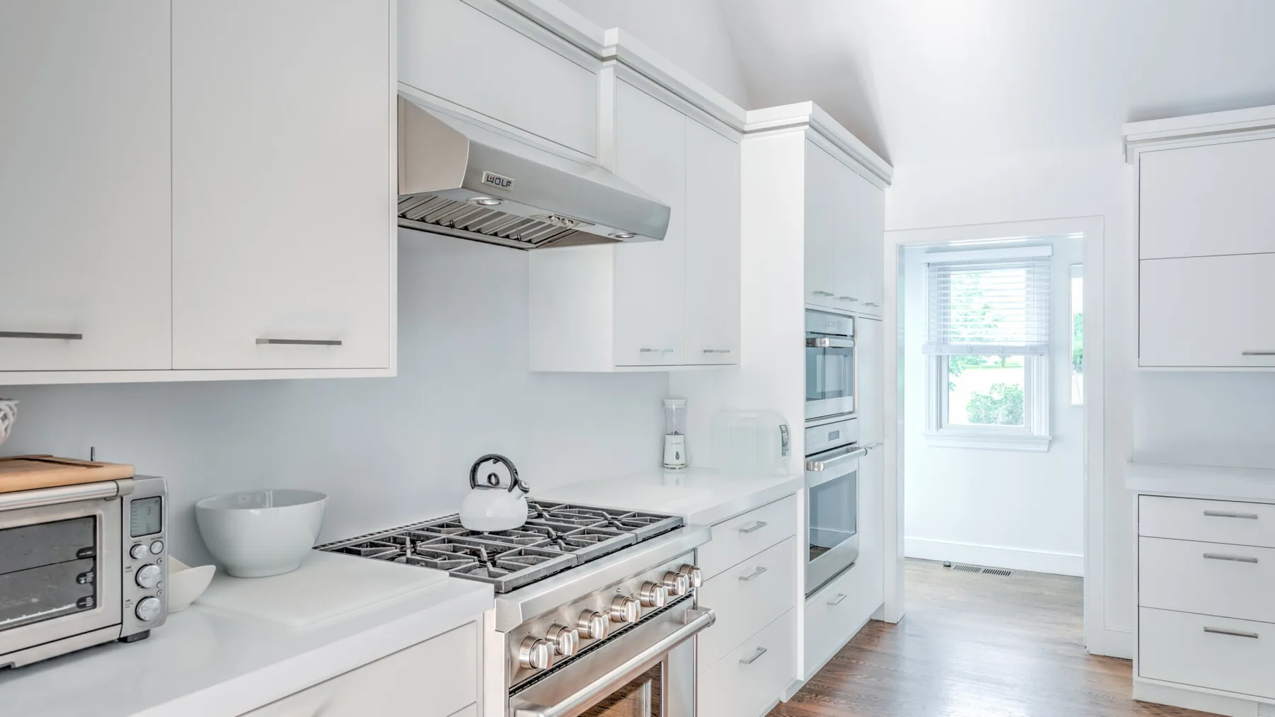 Una cocina blanca y luminosa con una estufa de gas, campana y electrodomésticos empotrados.