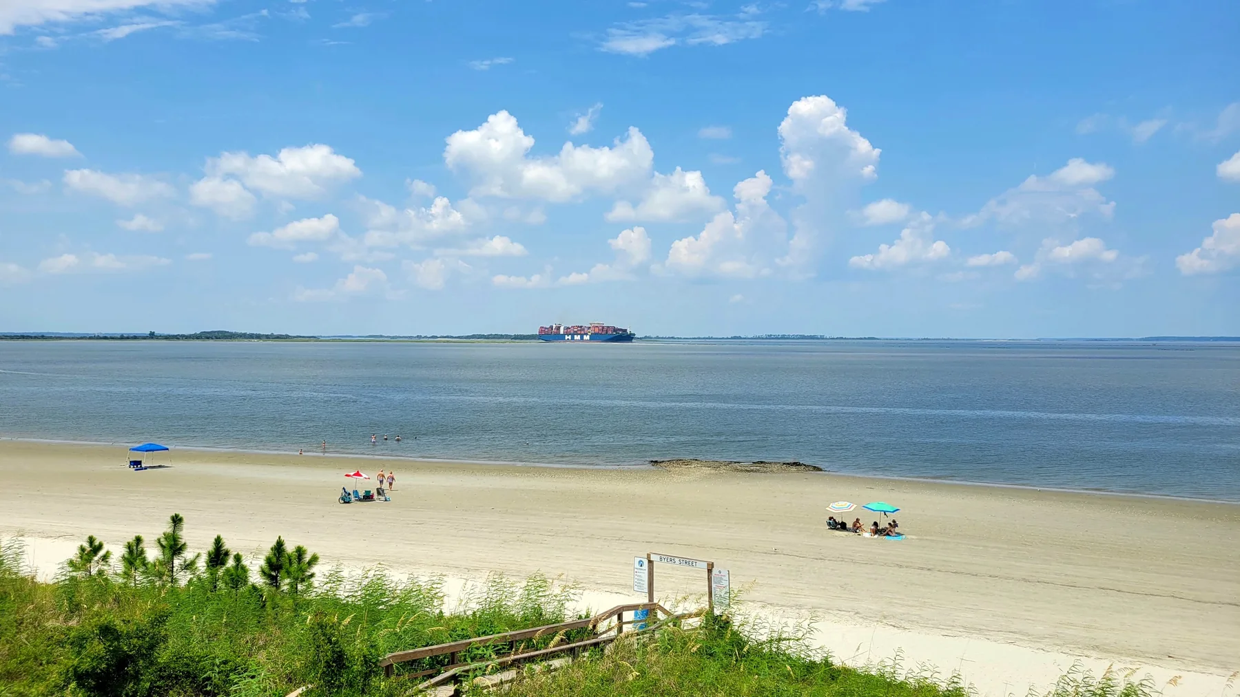 A sandy beach meets calm water beneath a partly cloudy sky.
