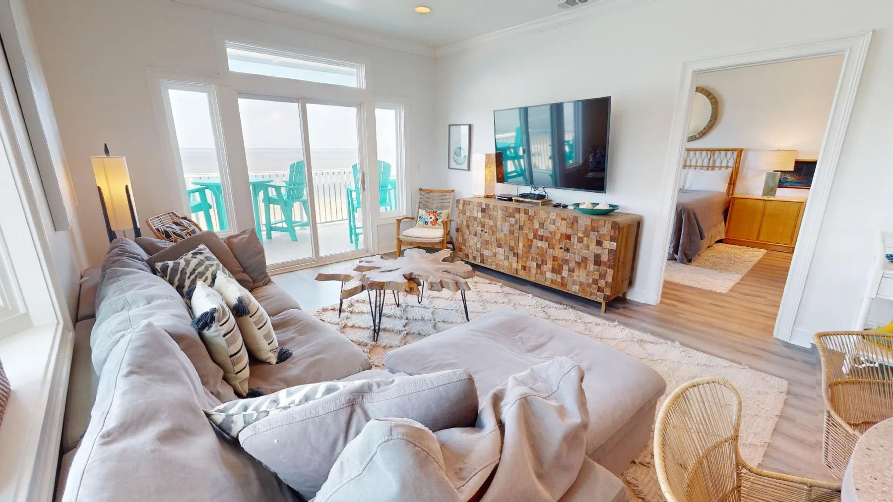 A bright living room has a sectional seating area, television, and glass doors opening to a balcony.