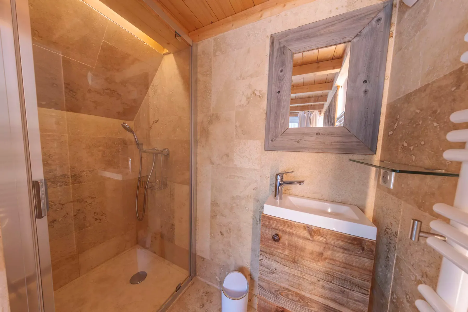 A bathroom with a glass shower, a sink, and a wood-framed mirror.