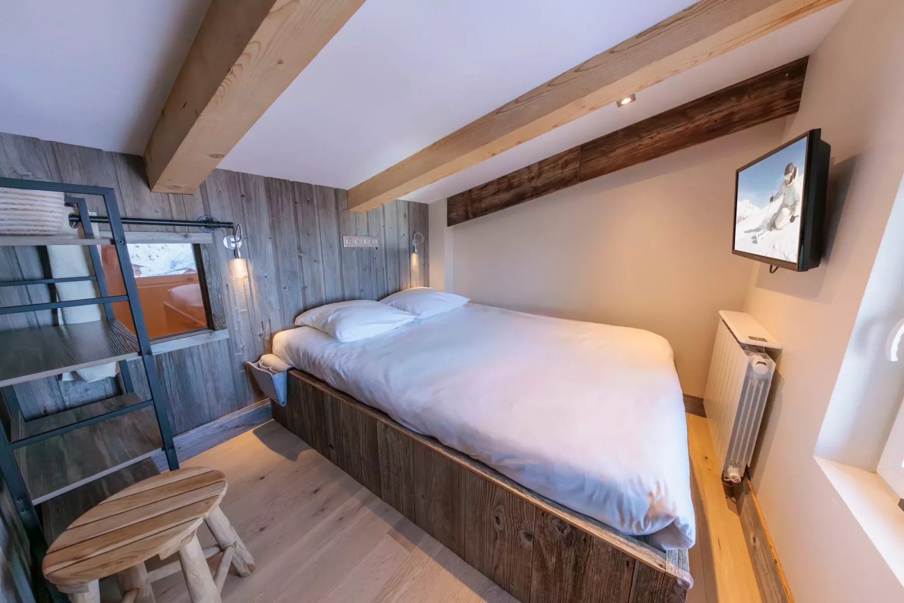 A bedroom with a bed beneath exposed wooden ceiling beams.