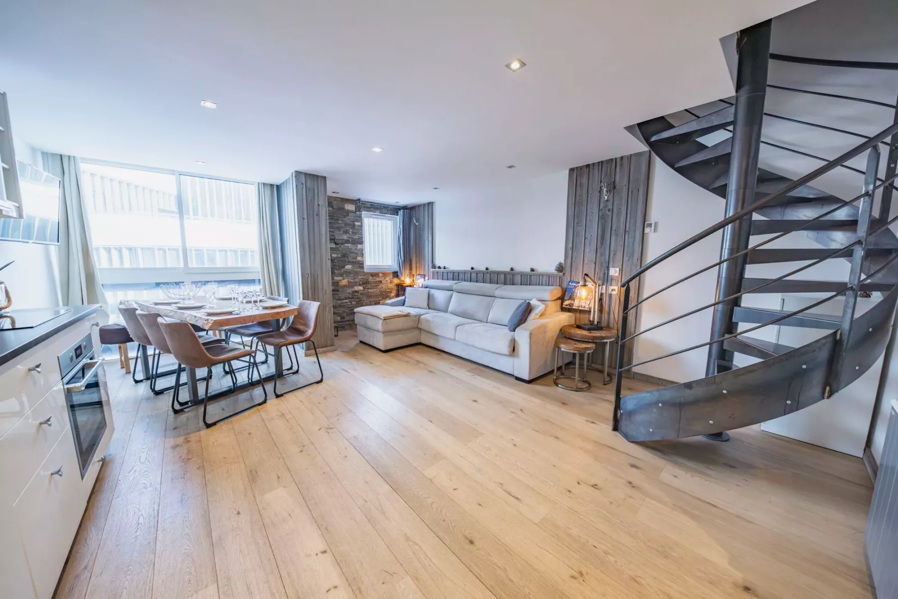An open living and dining area with a sectional seating area and a spiral staircase.