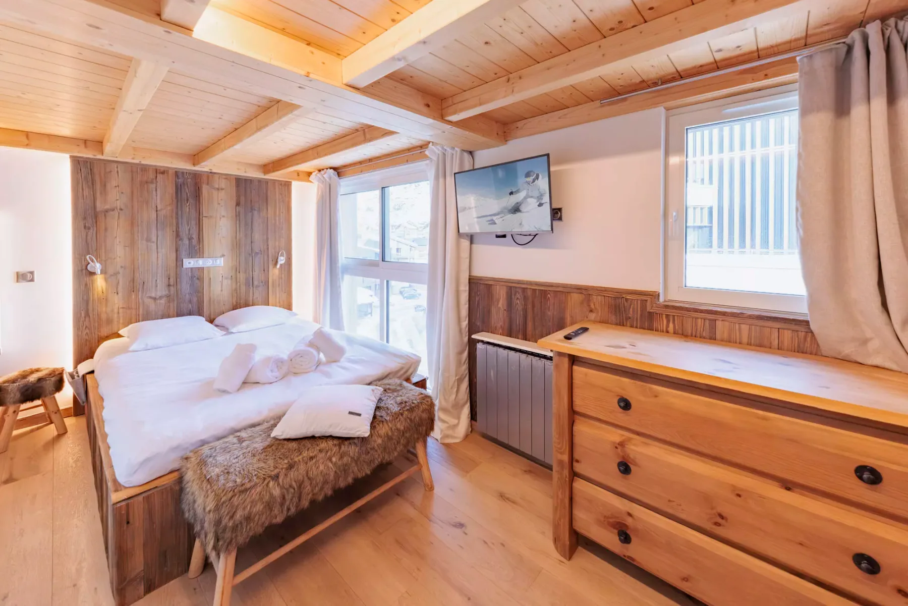 Un dormitorio con una cama, una cómoda de madera y ventanas.