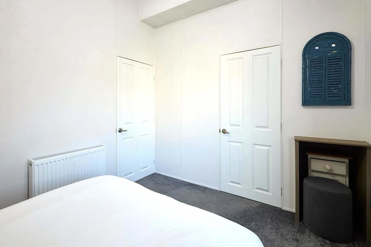 Un dormitorio con una cama, puertas blancas y una alfombra oscura.