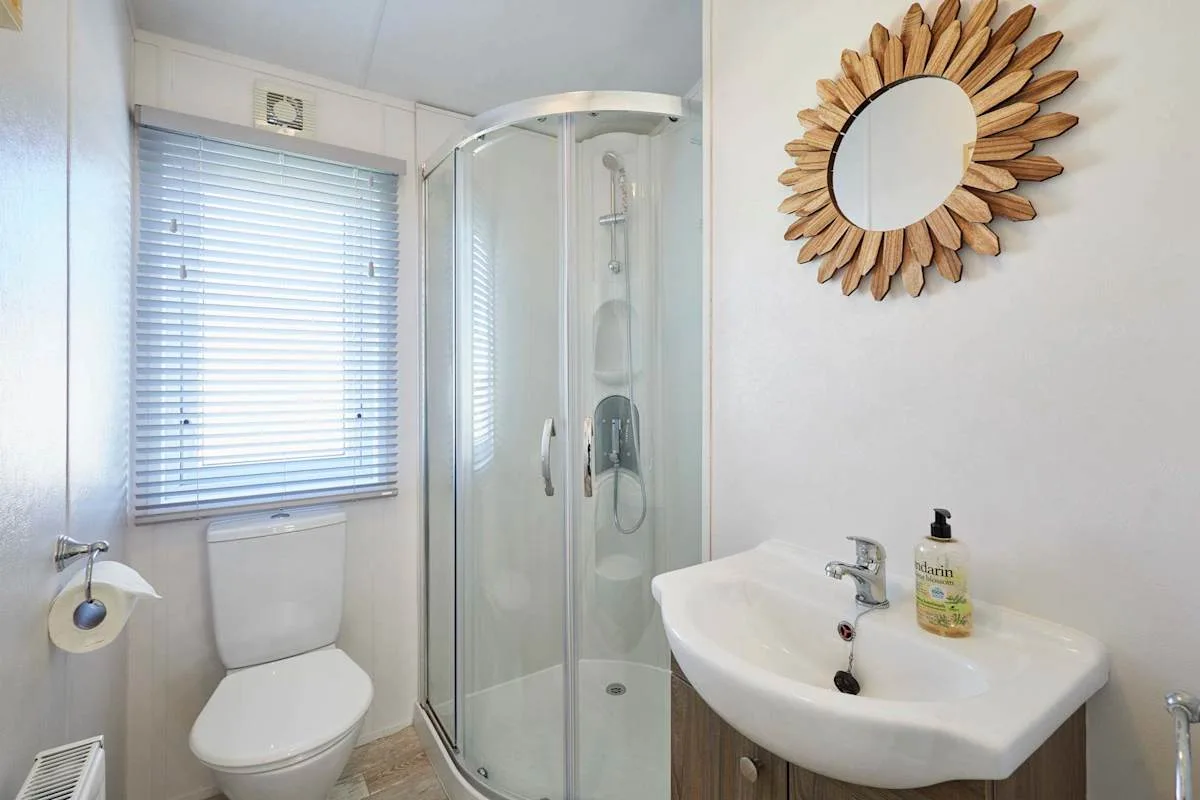 Un baño con ducha, inodoro y lavabo bajo un espejo redondo.