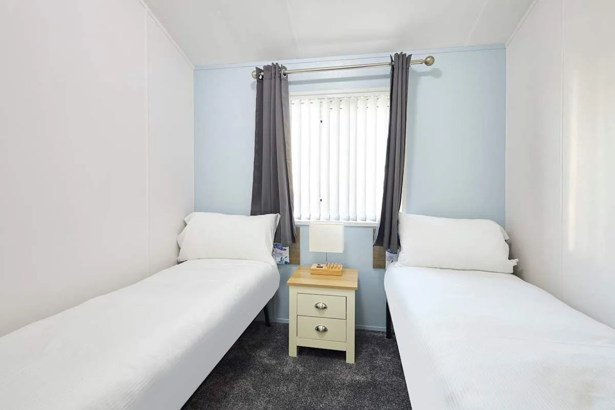 Un dormitorio con dos camas individuales y una mesita bajo la ventana.