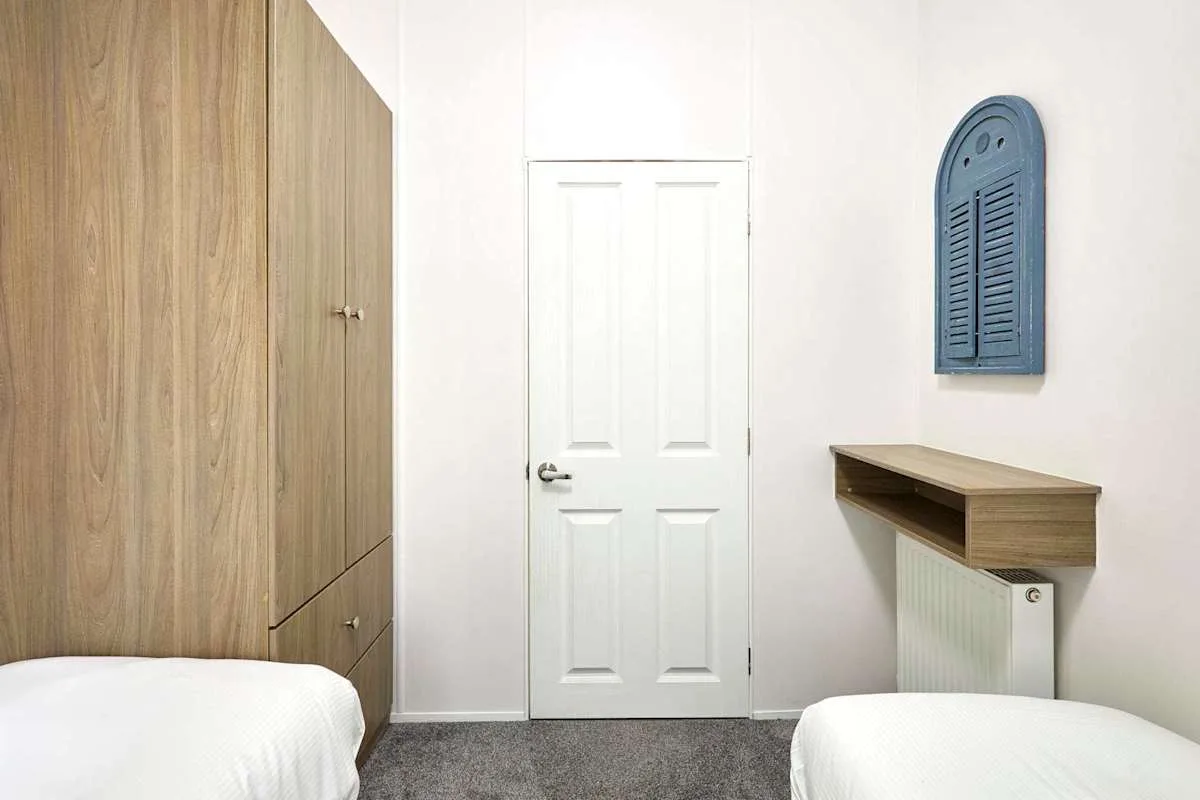 Un dormitorio luminoso con una puerta blanca, armarios de madera y dos camas.