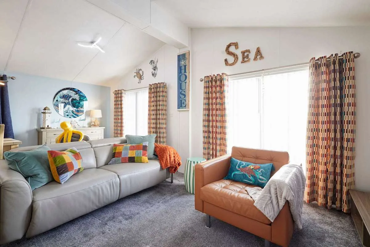 Una sala luminosa con asientos grises, un sillón naranja y cortinas estampadas.