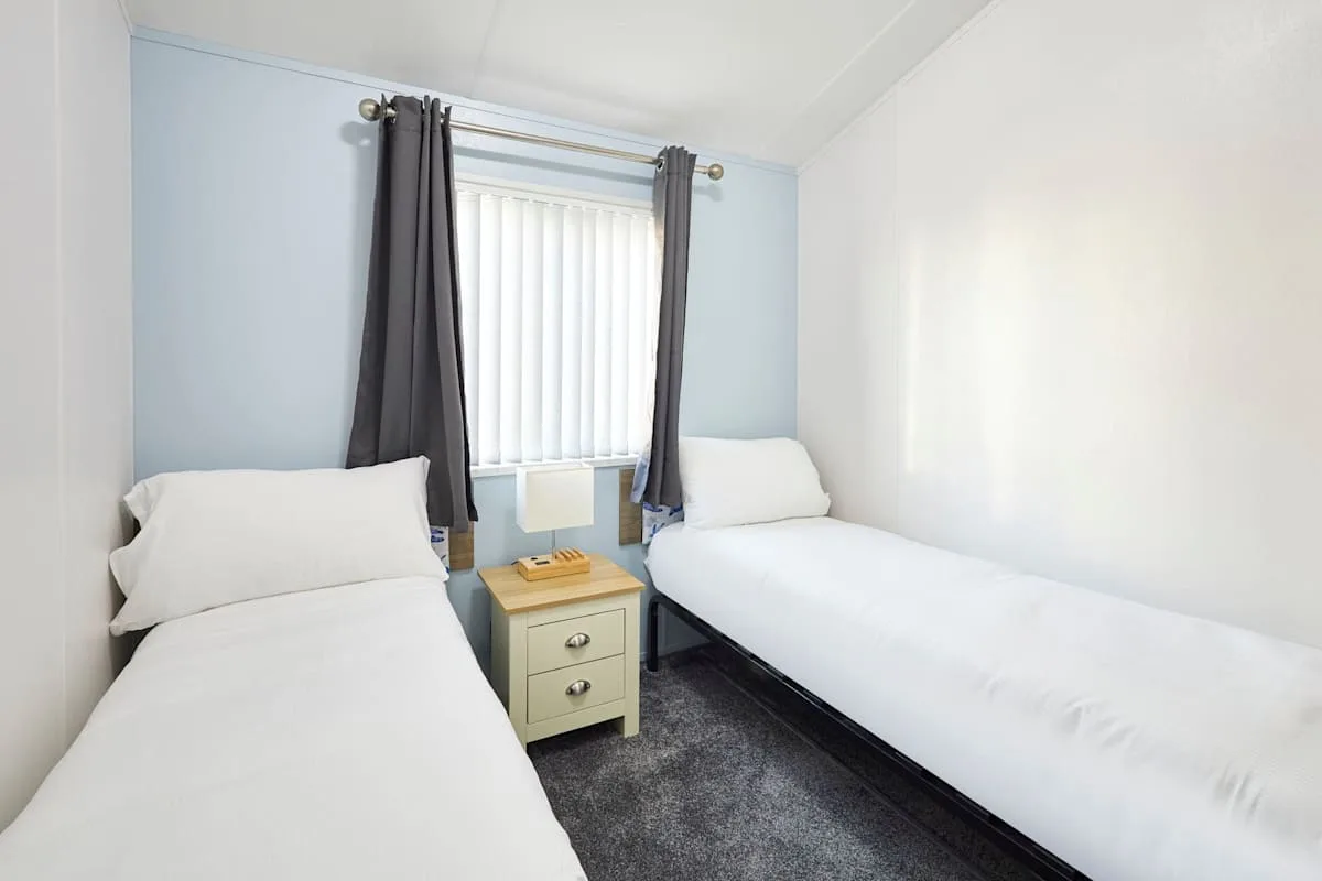 Un dormitorio con dos camas individuales y una ventana con persianas verticales.