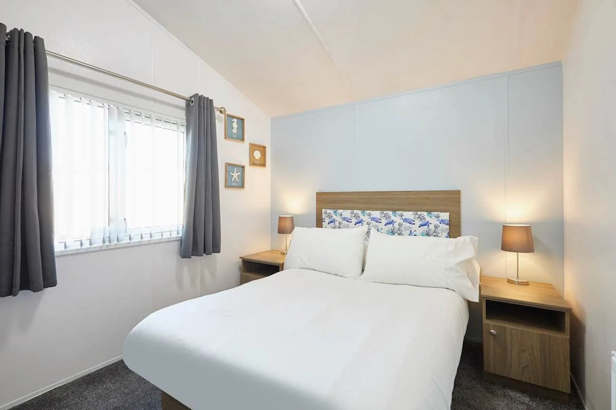 Un dormitorio con una cama, mesas de noche y una ventana con cortinas.