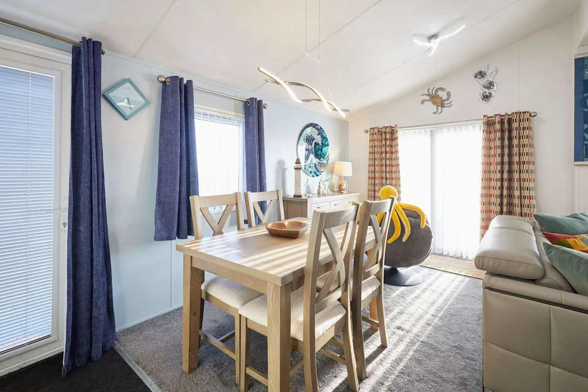 Comedor con una mesa de madera junto a una luminosa zona de estar.