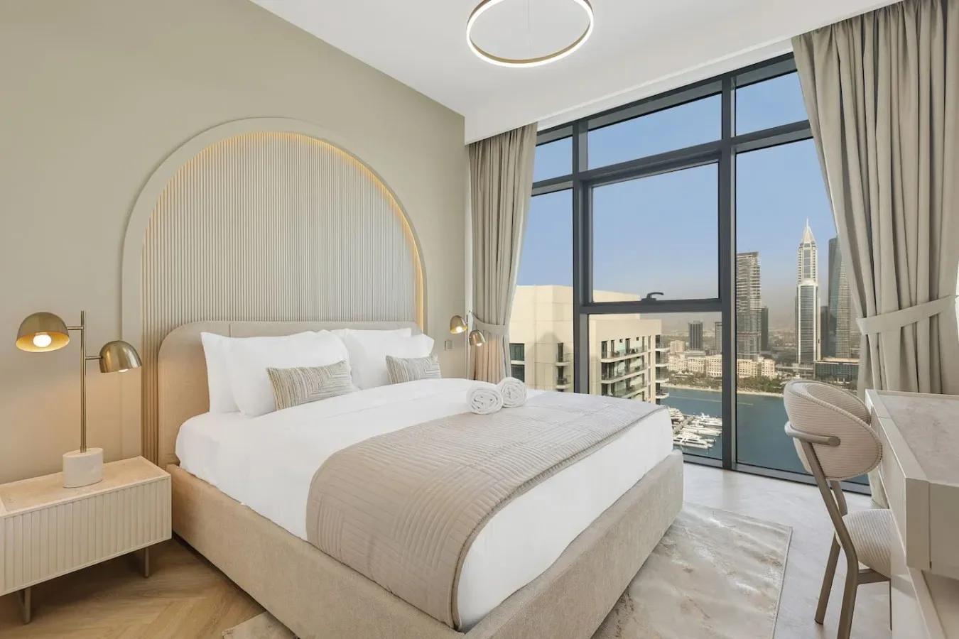Un dormitorio luminoso con una cama grande junto a ventanales con vistas a la ciudad.