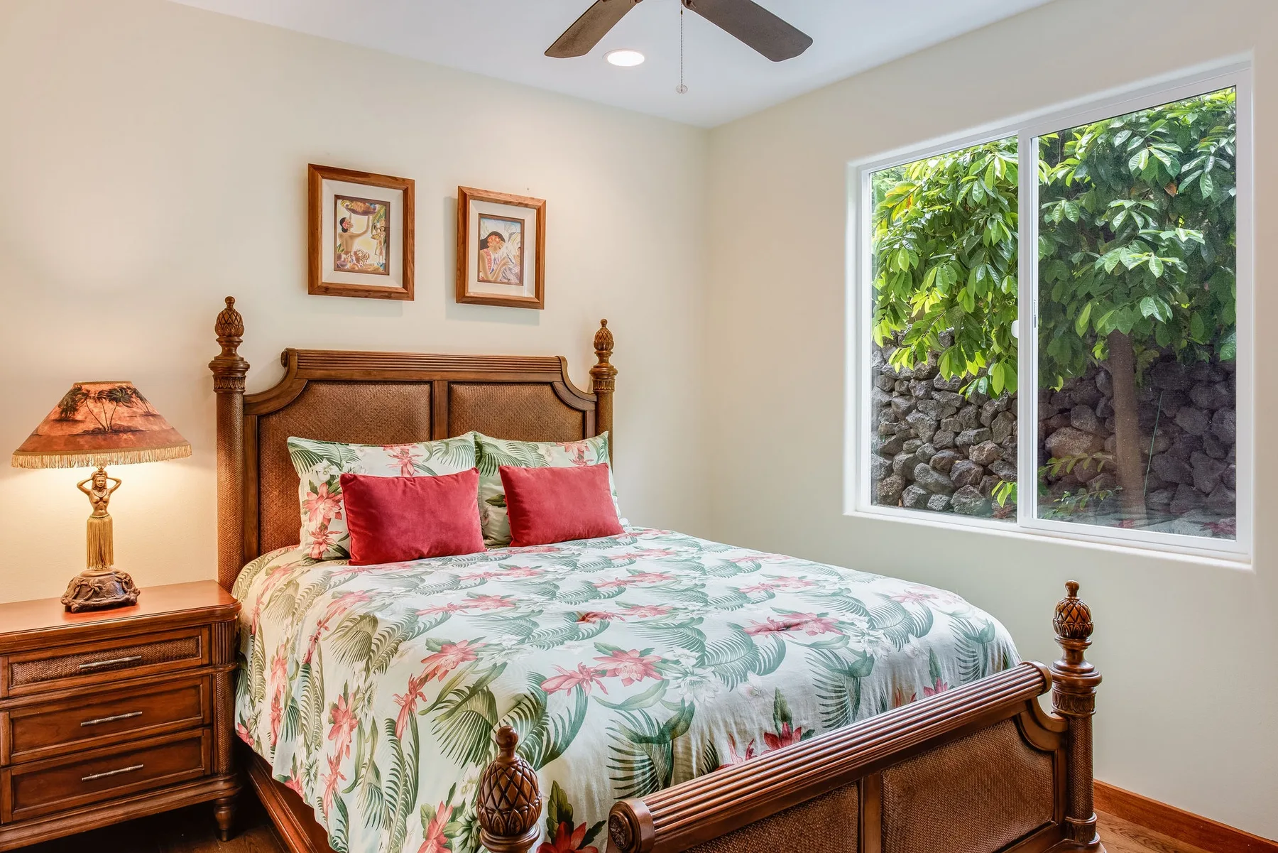 Un dormitorio con una cama de madera, ropa de cama floral y una ventana con vista a la vegetación.