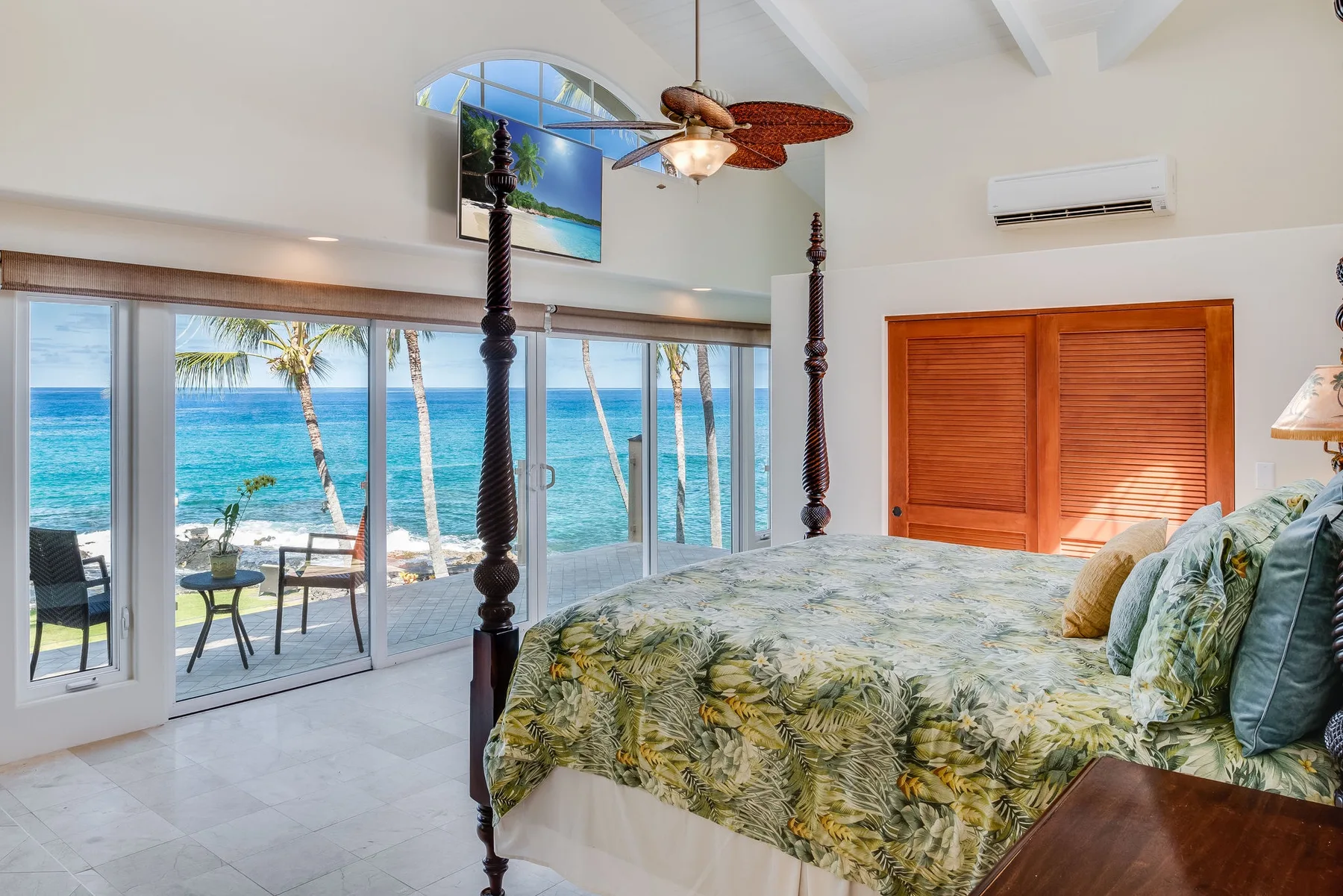 Un dormitorio con una cama grande junto a puertas corredizas de vidrio con vistas al mar.