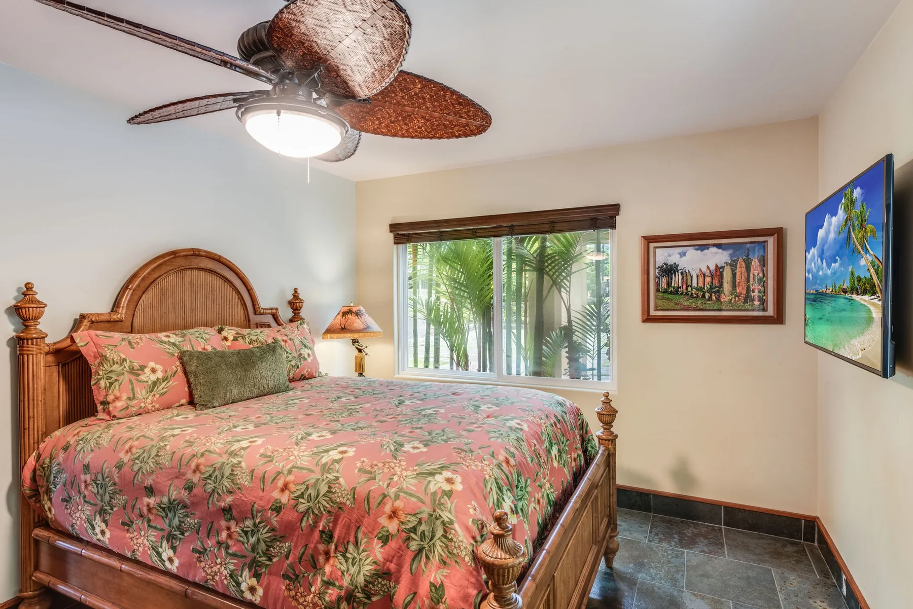 Un dormitorio con una colcha floral, una ventana y cuadros enmarcados.