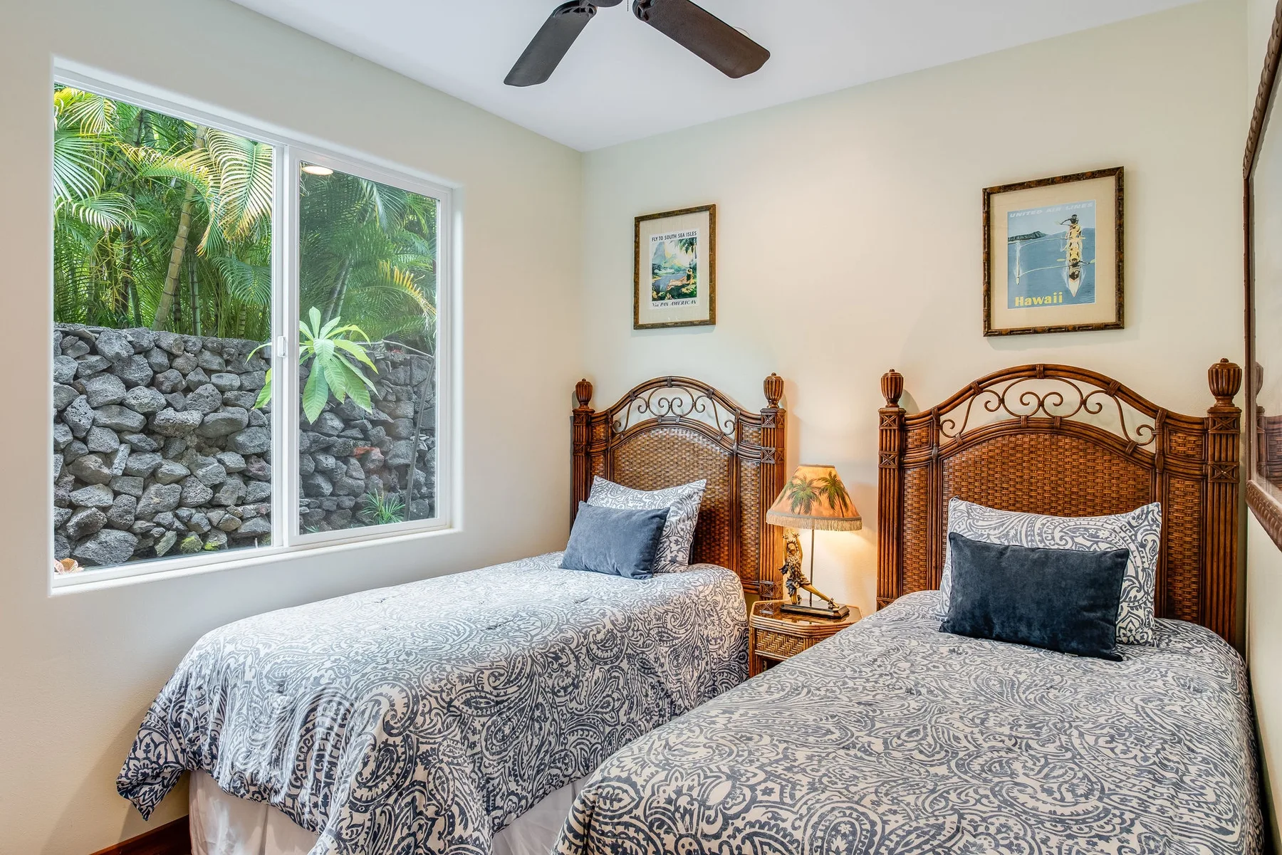 Un dormitorio con dos camas, ropa de cama estampada y una ventana grande con vistas a la vegetación.