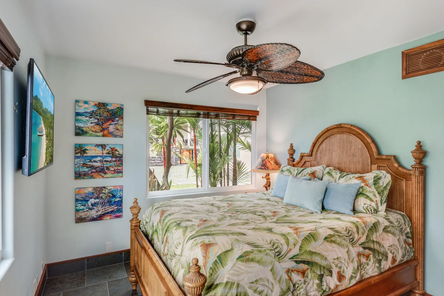 Un dormitorio con una cama de madera, ropa de cama con hojas y una ventana con palmeras.