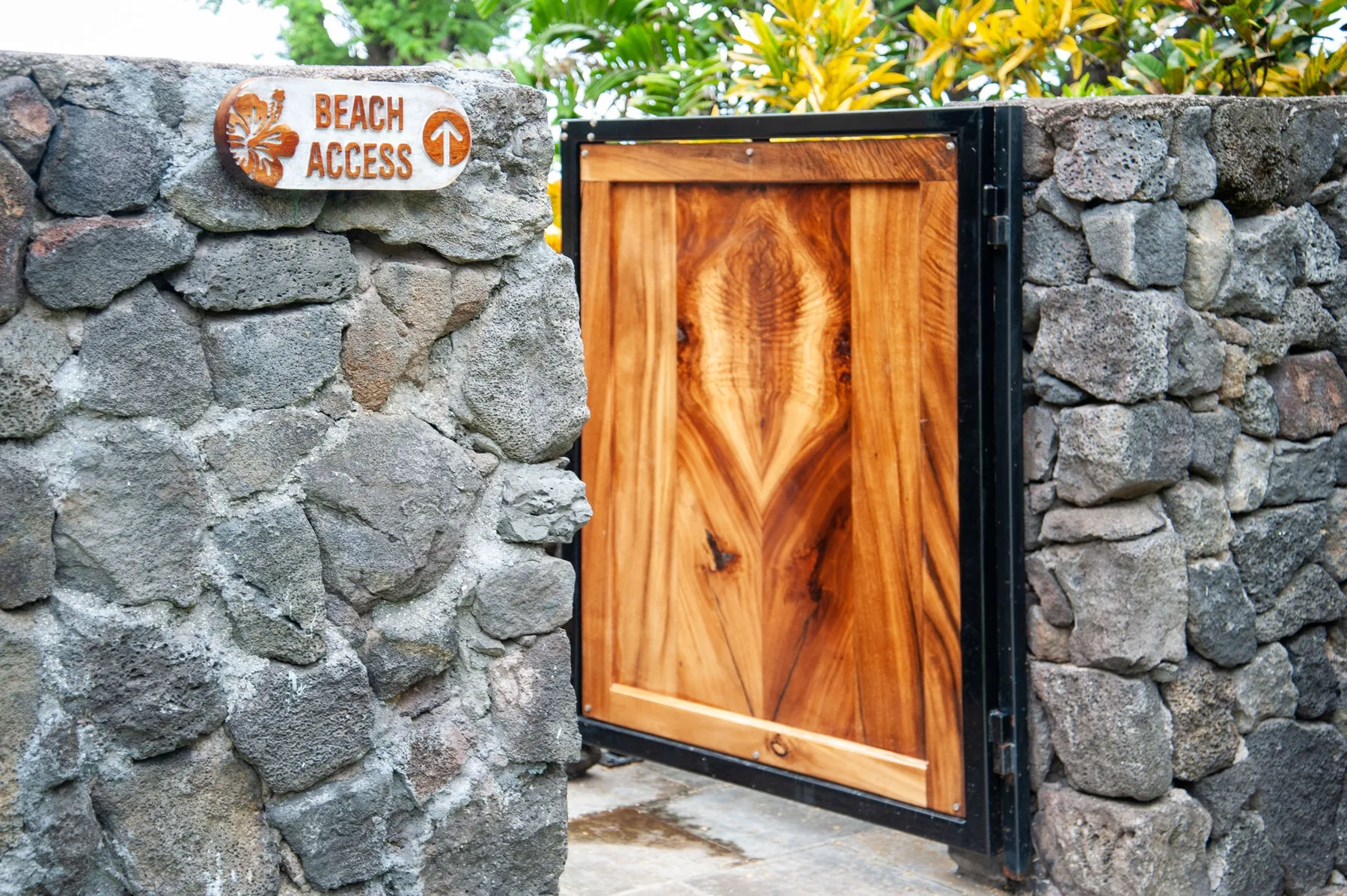Una puerta de madera se encuentra en un muro de piedra bajo follaje tropical.
