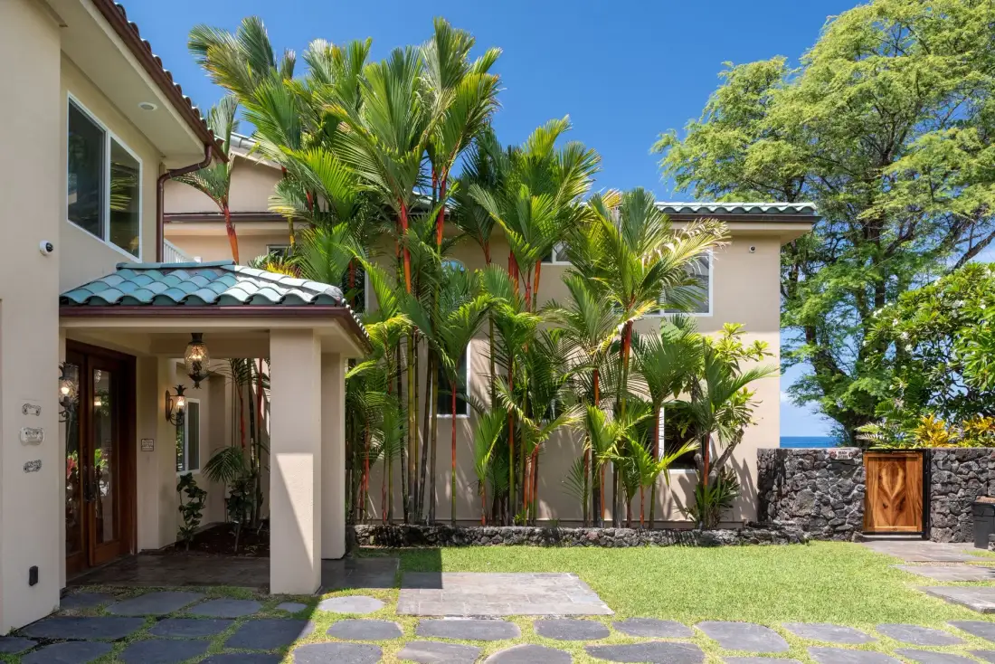 La entrada de una casa tropical da a un patio empedrado bordeado de palmeras.