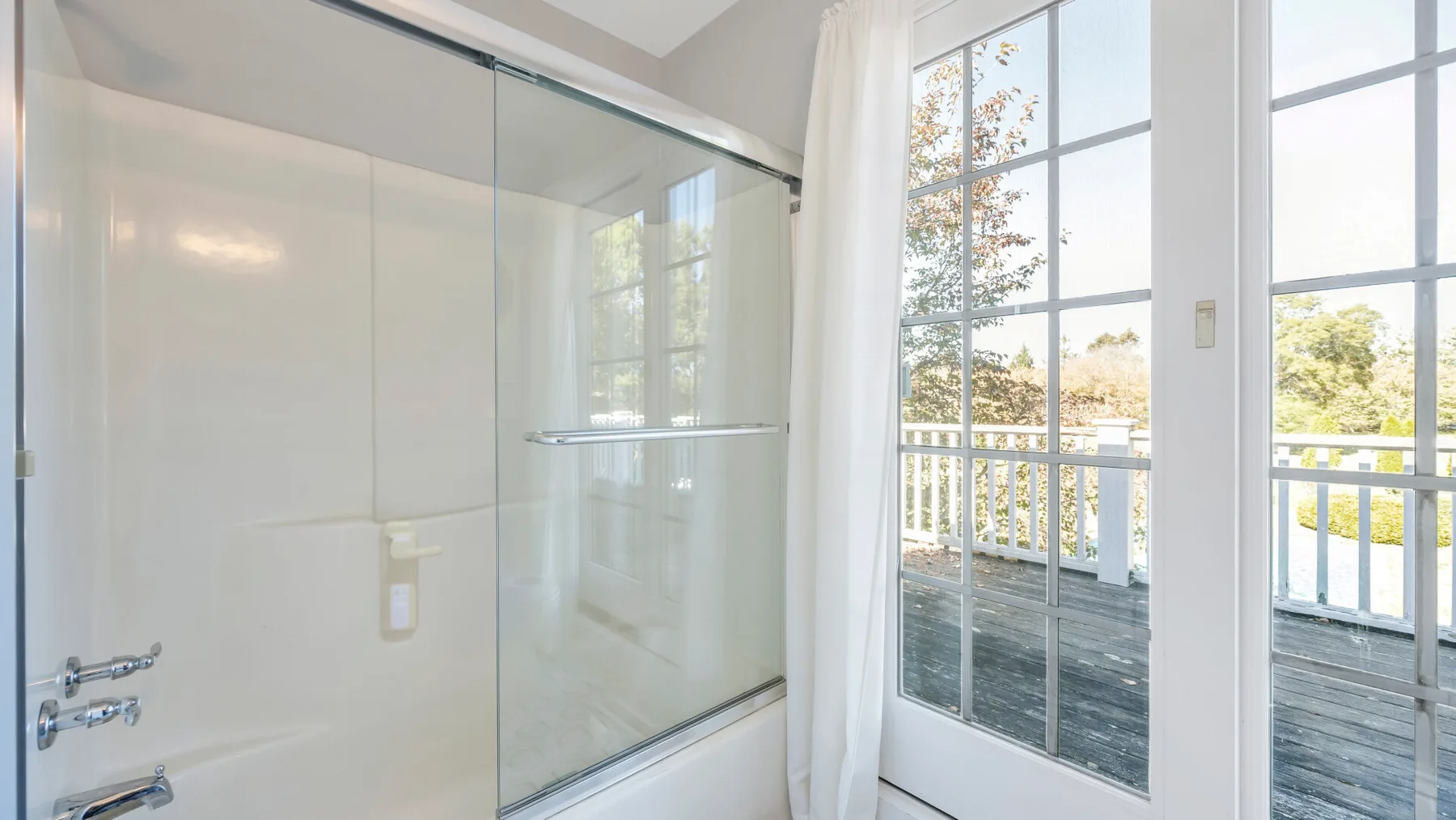 A bathroom with a glass shower beside large windows overlooking a deck.