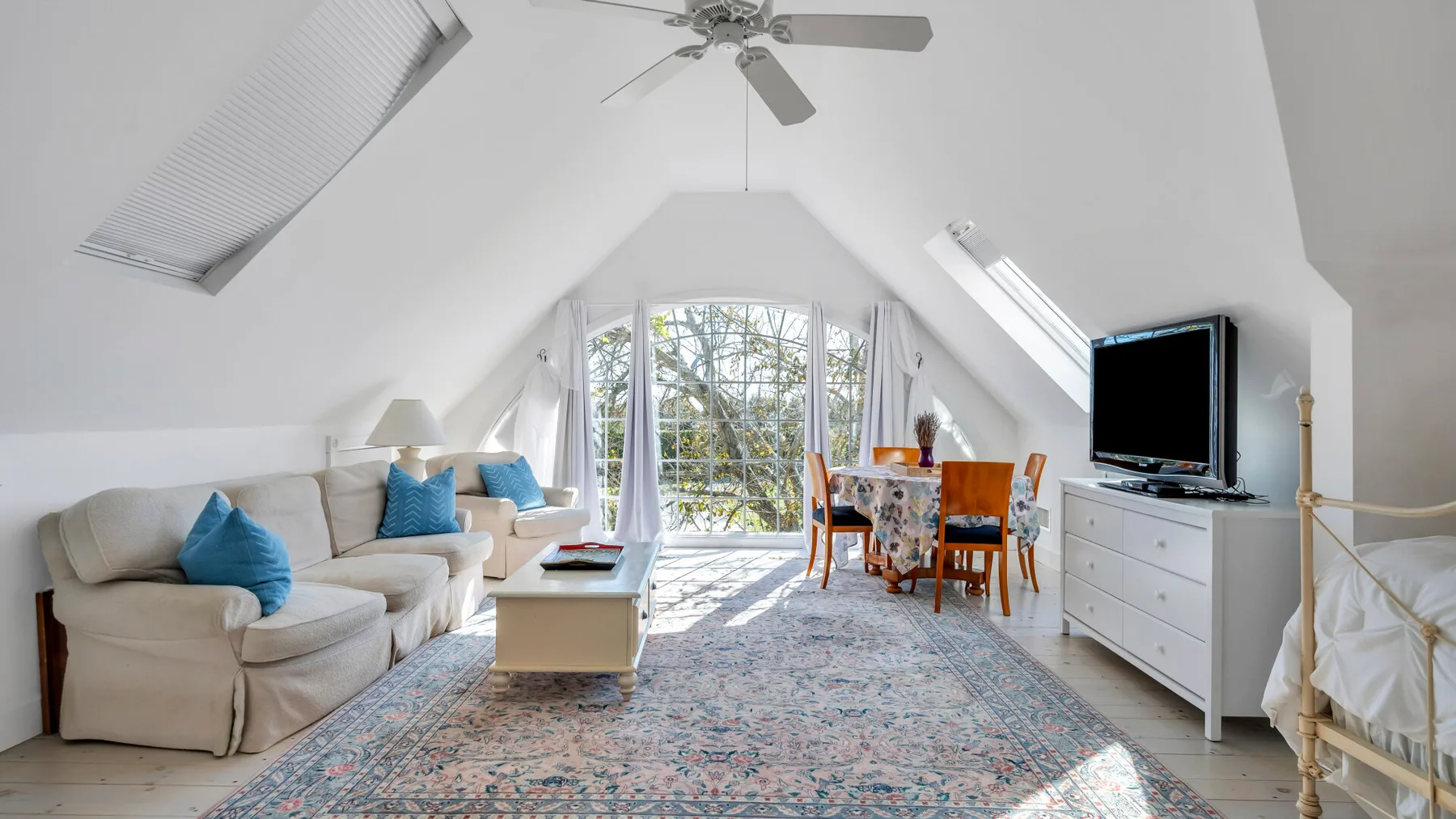 A bright attic living room with seating, a dining table, and large windows.