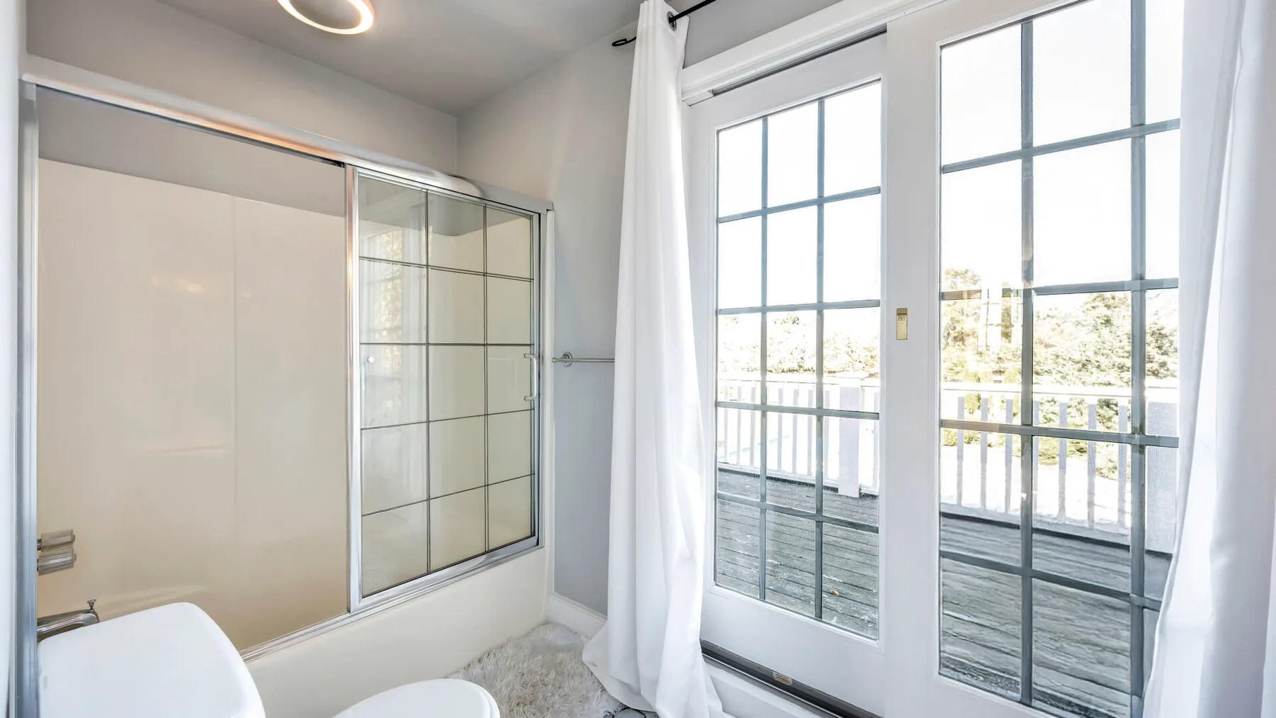 A bright bathroom with a glass shower enclosure and tall windows.