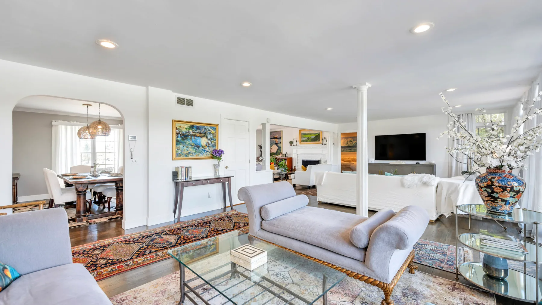 A bright living room with seating, glass tables, and colorful rugs.