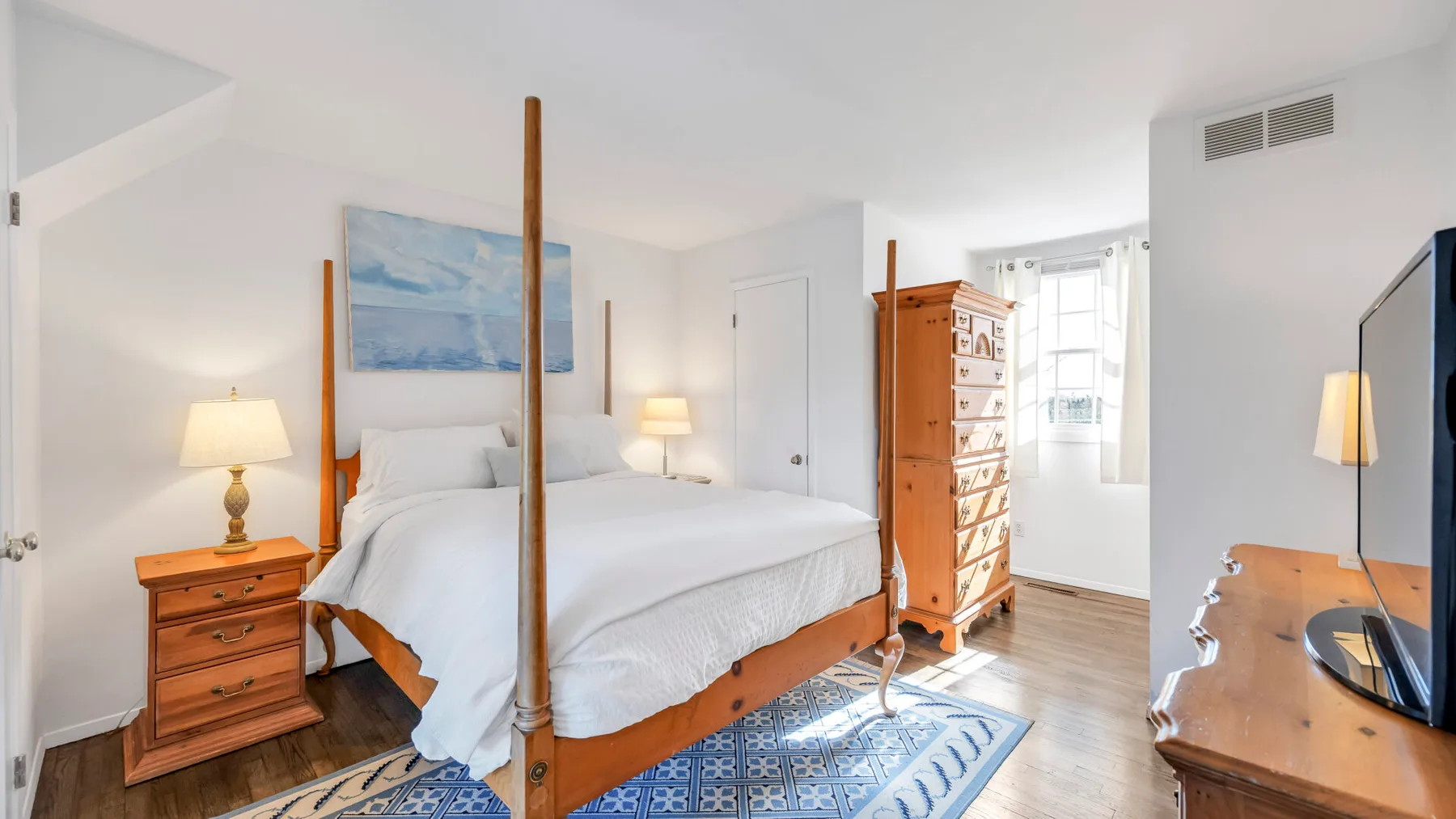 A bright bedroom with a four-poster bed and wooden furnishings.