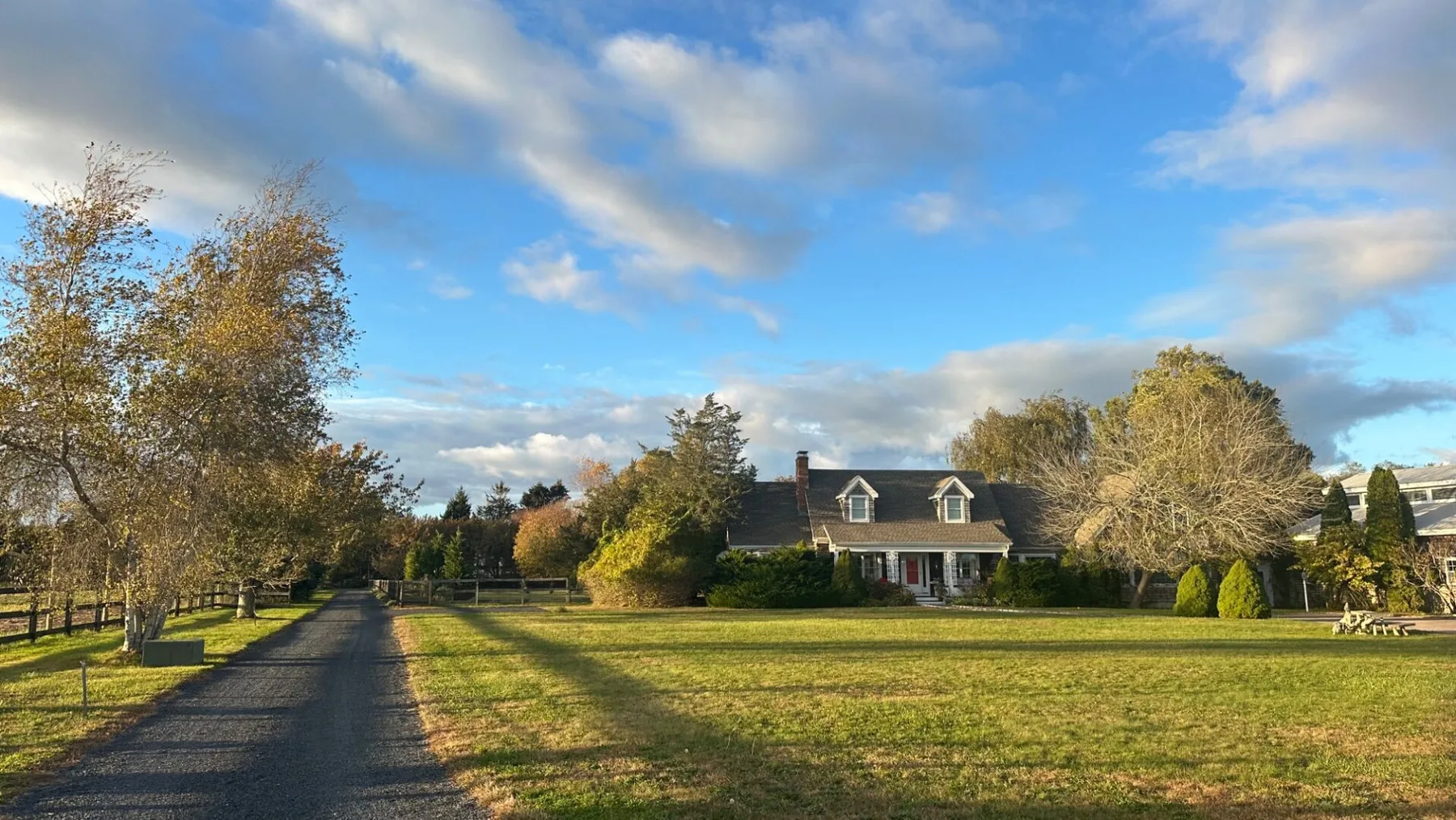 A house stands beyond a broad grassy lawn, with trees lining the driveway.