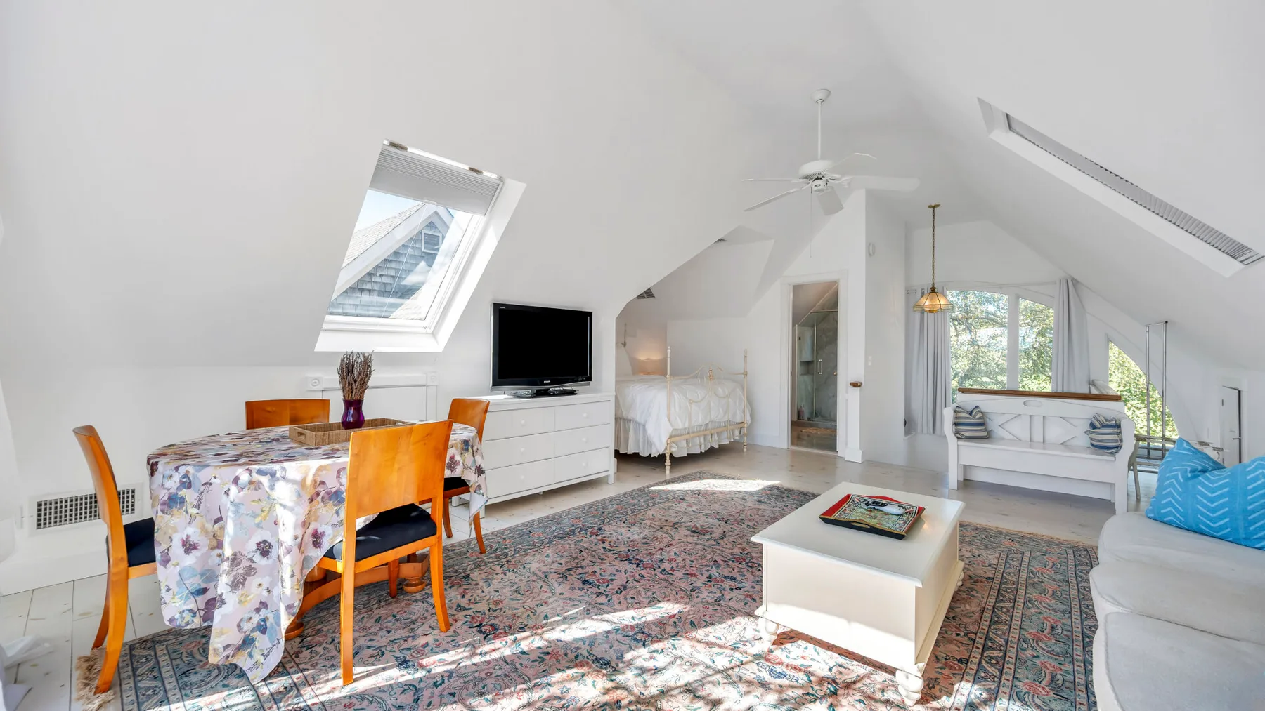 A bright attic bedroom with a dining table, bed, and skylights.