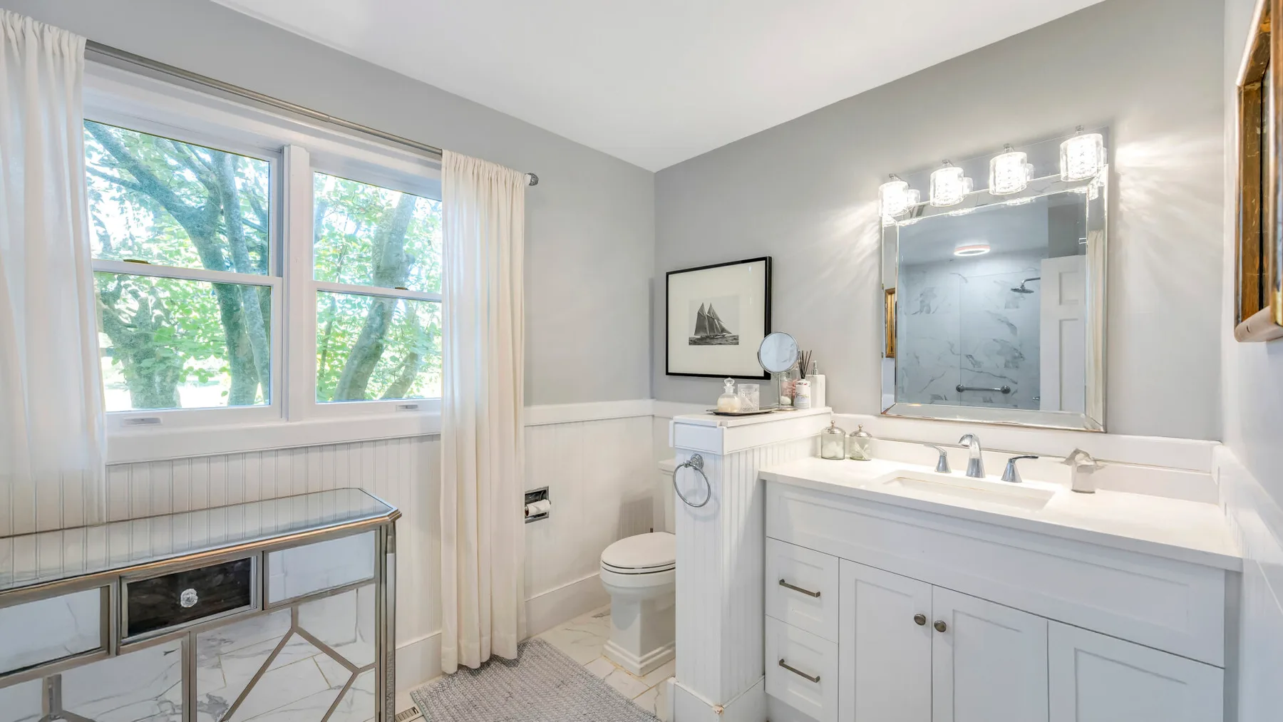 A bright bathroom with a vanity, mirror, and large windows.
