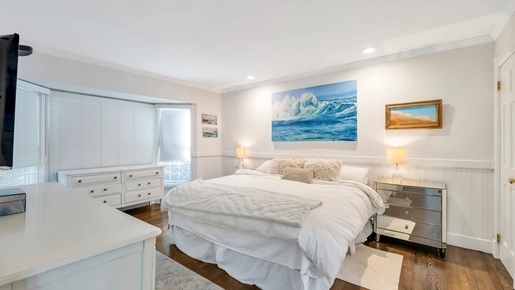 A bright bedroom with a large bed, bedside lamps, and ocean-themed wall art.
