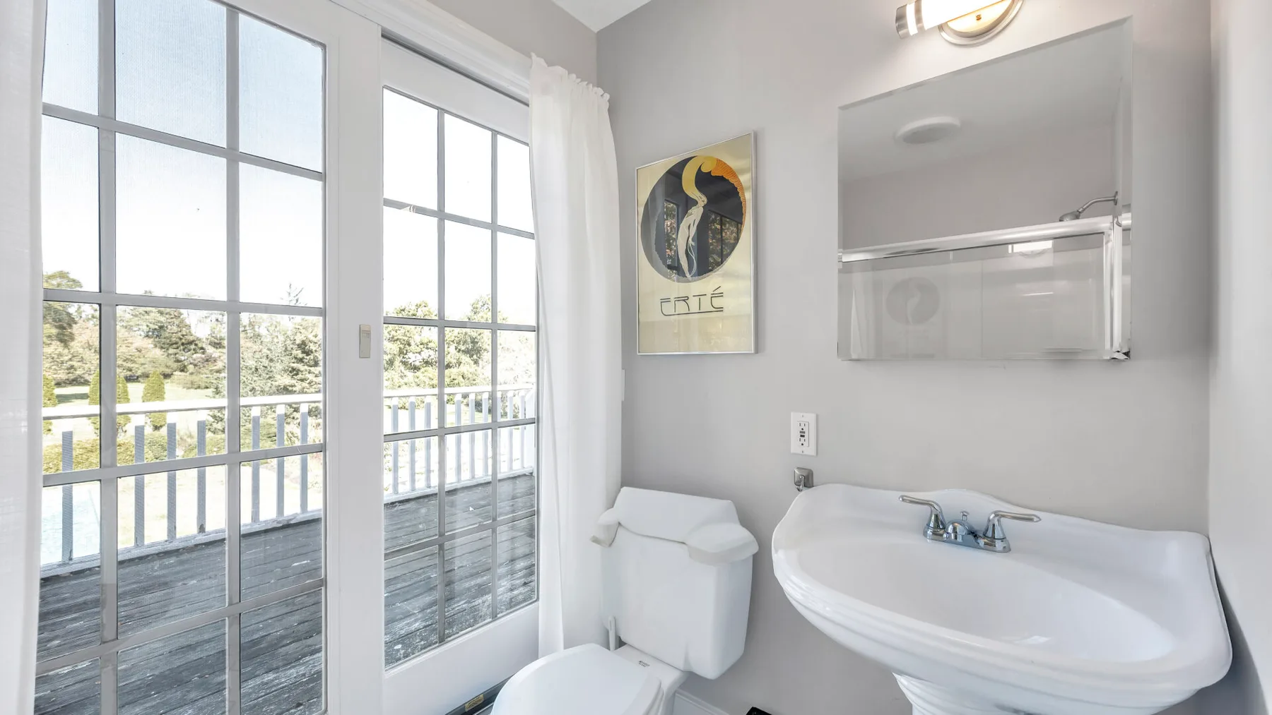 A bright bathroom with a sink, toilet, and glass doors opening onto a balcony.