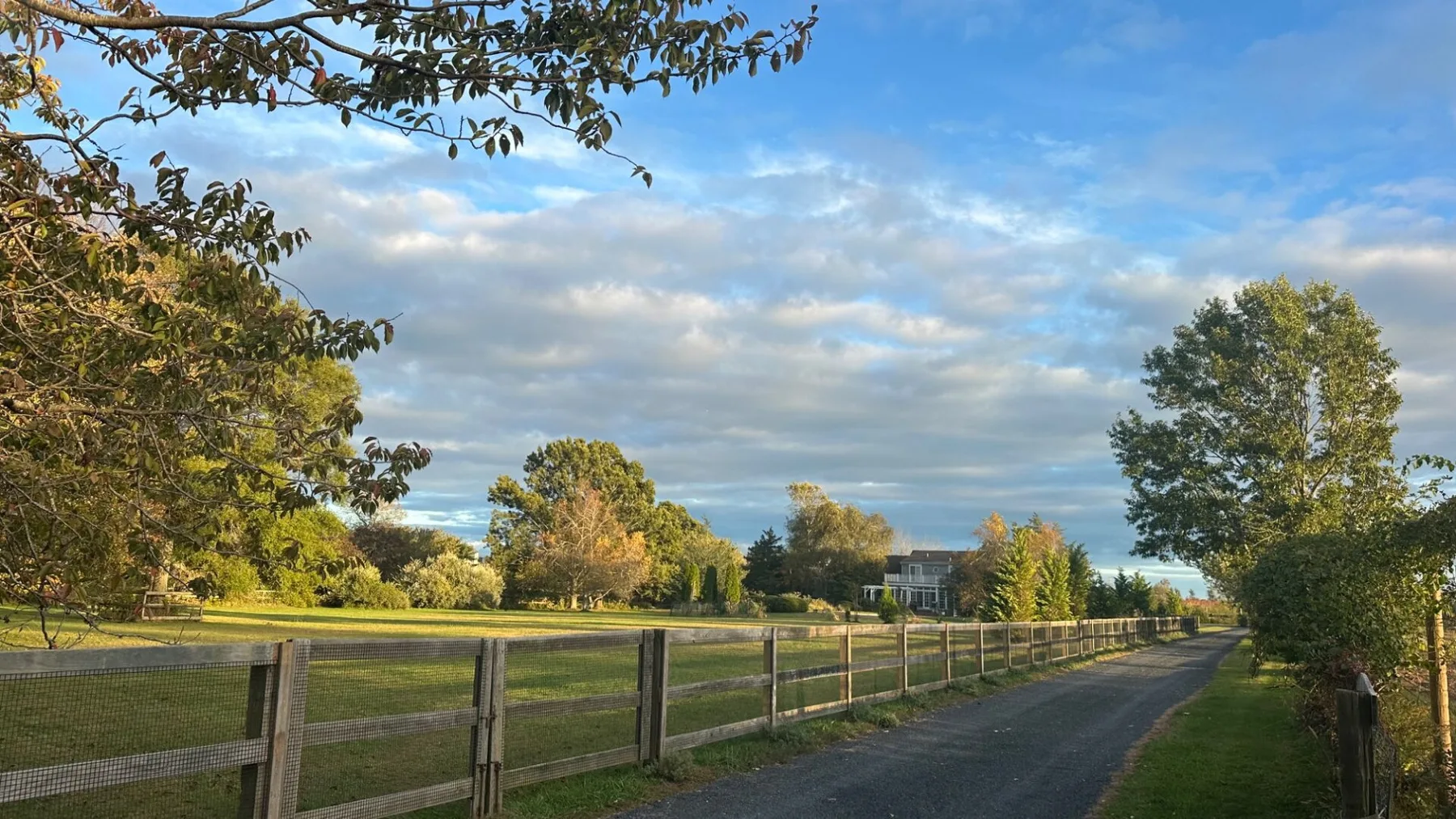 A paved path runs beside a fenced grassy field beneath a cloudy sky.